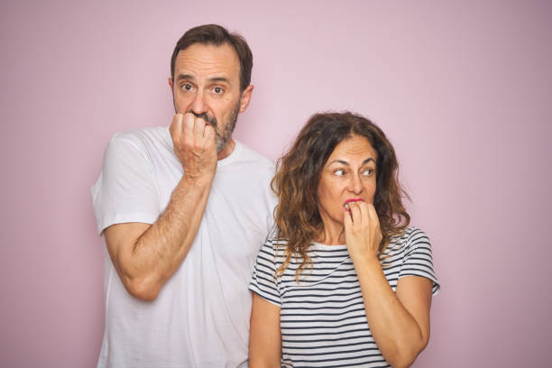 istock Beautiful middle age couple together standing over isolated pink background looking stressed and nervous with hands on mouth biting nails. Anxiety problem. 1174146883