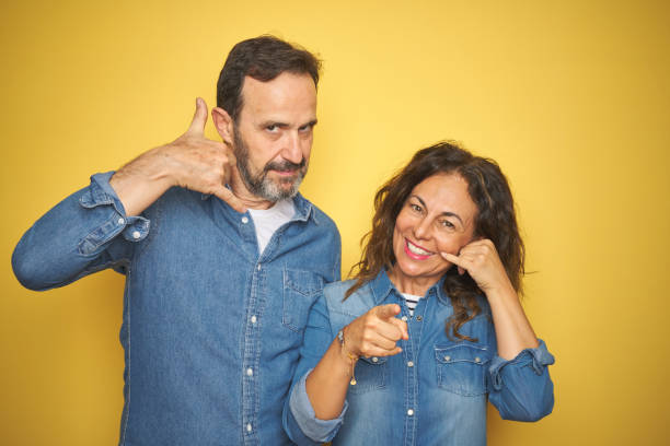 istock Beautiful middle age couple together standing over isolated yellow background smiling doing talking on the telephone gesture and pointing to you. Call me. 1174148572
