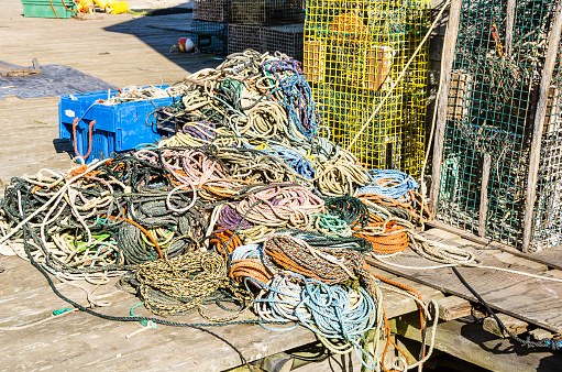 Heap of colourful mooring ropes on a wooden pier in a fishing harbour. Lobster pots are visible in background.