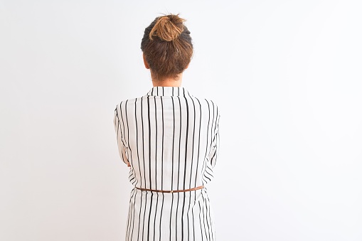 Middle age businesswoman wearing striped dress and glasses over isolated white background standing backwards looking away with crossed arms