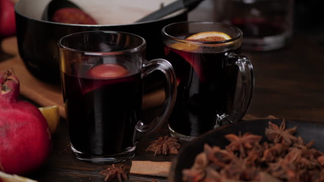 Female hands put slices of oranges and anise stars in clear glass mugs with mulled wine. Close up slider movement.