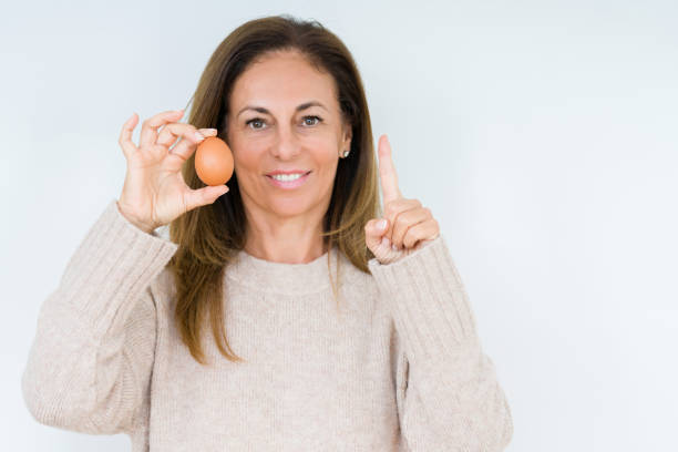 istock Middle age woman holding fresh egg over isolated background surprised with an idea or question pointing finger with happy face, number one 1174156232