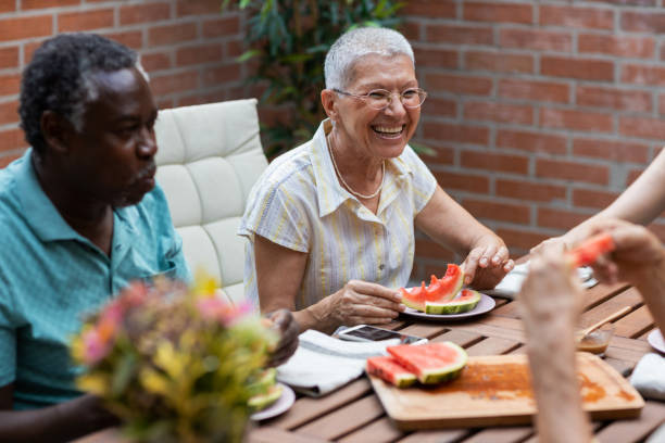 Seniors Enjoying In Vegan Dinner Group of senior friends enjoying in vegan meal in backyard. Eating watermelon and talking. black man eating watermelon stock pictures, royalty-free photos & images