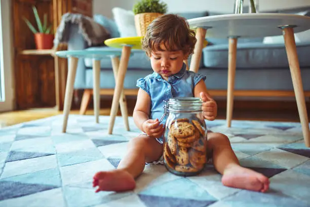 Photo of Beautiful toddler child girl holding jar of cookies sitting on the floor