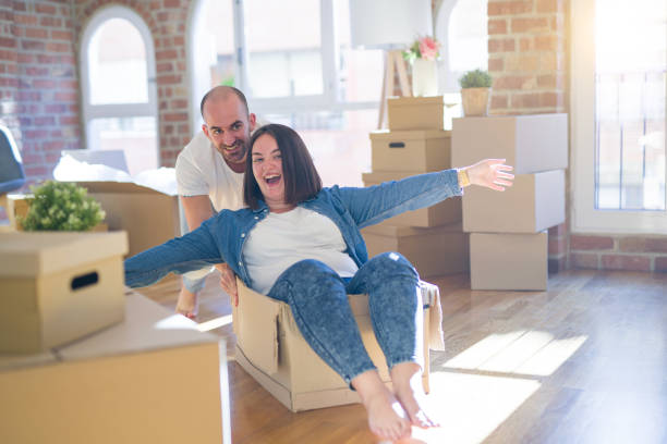 istock Funny and crazy couple having fun riding a cardboad box as a car, smiling happy and lauging at new home 1174172346