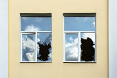 The glass of broken windows reflects the sky, a house with broken windows close up.