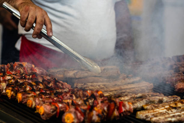 chef che prepara carne su una griglia a carbone, bistecche di maiale, petto di pollo, salsicce, pezzi di braciole di carne in un festival di cibo di strada - tirgoviste foto e immagini stock