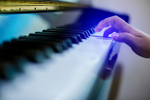 Blurry image of piano key with hand kid press it to play music.
