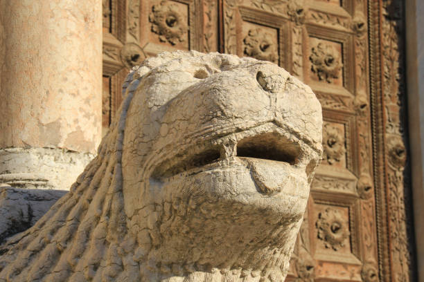 Statue of a lion and an old man holding up a column in Ferrara (Emilia-Romagna, Italy). On the background the facade of the Cathedral of the city.