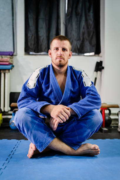 junge bjj brasilianischejiu jitsu oder judo-athlet jujitsu kämpfer sittin auf dem tatami-matten boden auf dem training tragen blau kimono gi - ju jitsu stock-fotos und bilder