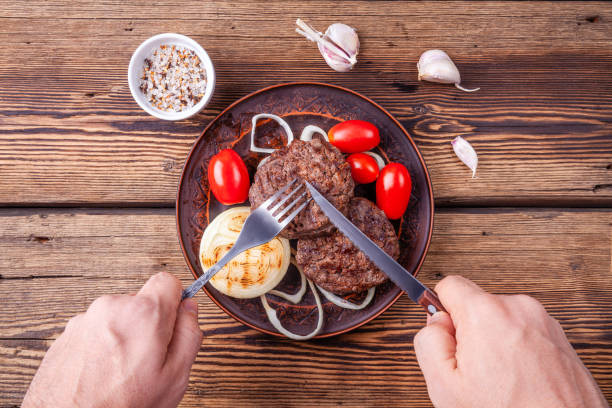 istock Cooked burger meat on wooden background with mens hands with fork and knife 1174232390