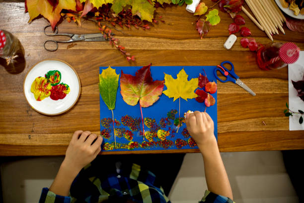istock Children, applying leaves using glue, scissors, and paint, while doing arts and crafts in school 1174235933