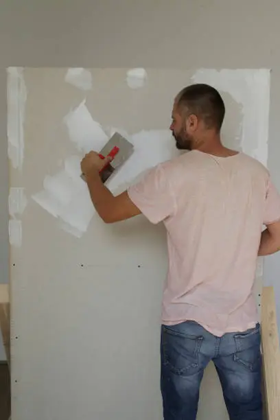 Man plastering wall with putty-knife. Fixing wall surface and preparation for painting. DIY housing improvement project.