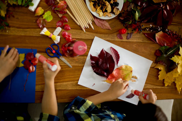 istock Children, applying leaves using glue, scissors, and paint, while doing arts and crafts in school 1174236712