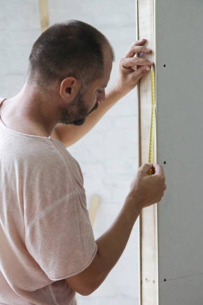istock Man holding a meter, measuring dimensions on plasterboard panel - DIY home improvement concept 1174236848