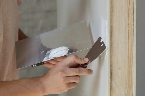 Man plastering wall with putty-knife. Fixing wall surface and preparation for painting. DIY housing improvement project.