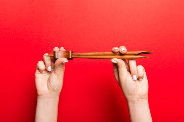 Crop image of two female hands holding chopsticks on red background. Ready to eat concept with copy space