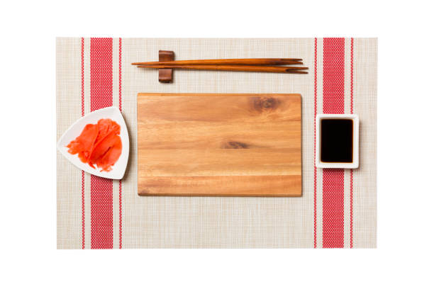 istock Empty rectangular brown wooden plate with chopsticks for sushi, ginger and soy sauce on sushi mat background. Top view with copy space for you design 1174240399