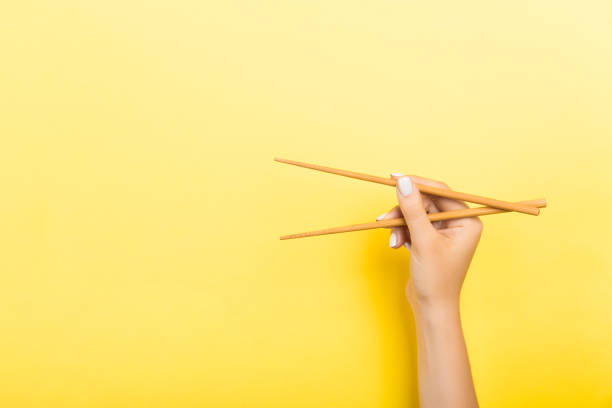 hölzerne essstäbchen mit weiblichen händen auf gelbem hintergrund. bereit für esskonzepte mit leerem raum - sushi japanese culture food domestic kitchen stock-fotos und bilder