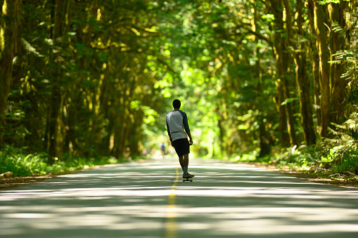 African American man skateboarding on a lush forested road. Full length of man skateboarding on road. Male is practicing sport in nature.