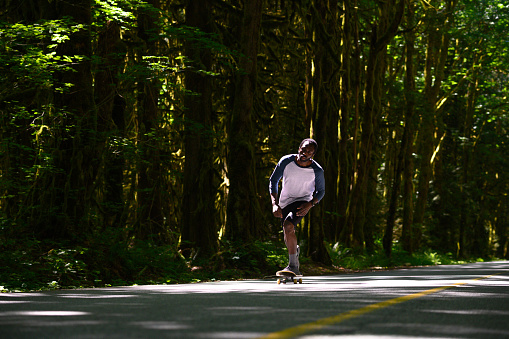 African American man skateboarding on a lush forested road. Full length of man skateboarding on road. Male is practicing sport in nature.