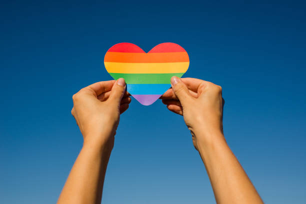 Woman holds in hands a heart in the colors of the rainbow. Young beautiful girl. LGBT history month. Pride Month. Lesbian Gay Bisexual Transgender. LGBT flag. Love, human rights, tolerance. LGBTQ+ stock photo