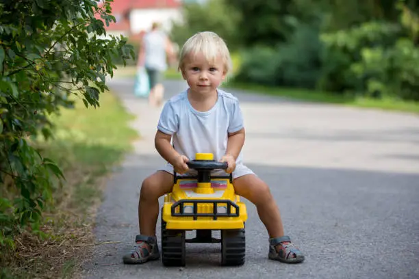 Sweet toddler boy, riding plastic toycar on the street in quiet neighborhood, summertime