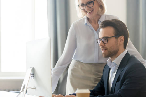 istock Smiling middle-aged businesswoman help male employee working on pc 1174254714