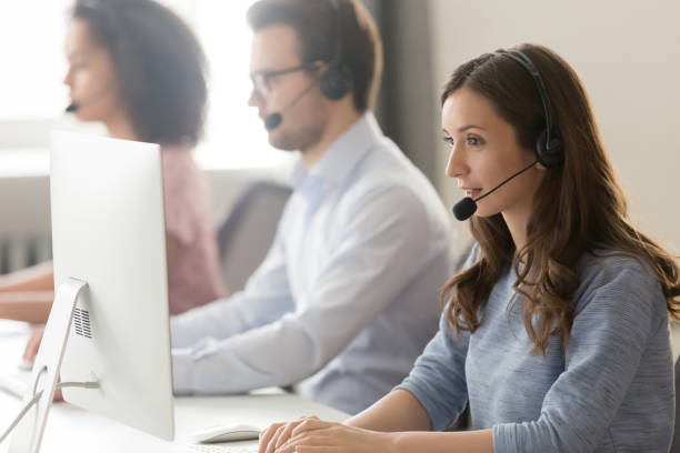 o agente fêmea nos auriculares consulta o cliente em linha usando o pc - stroking - fotografias e filmes do acervo