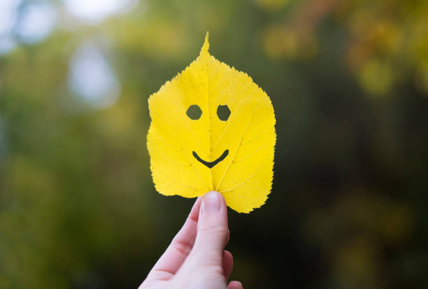 Autumn yellow leaf smiling emoji in a hand.