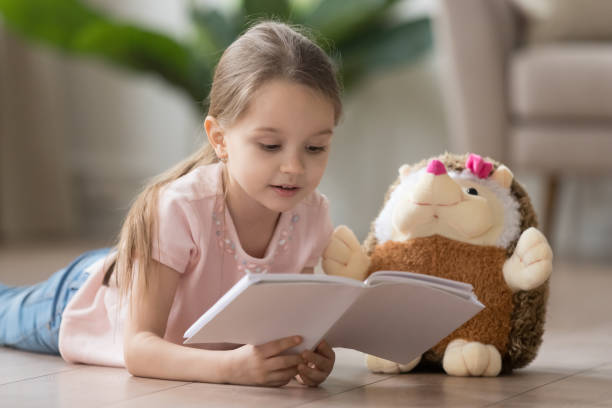 istock Cute little girl reading interesting book, lying on warm floor 1174255064