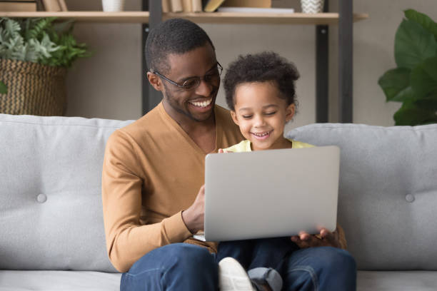 улыбаясь черный папа и маленький сын играть в компьютерные игры - video game family child playful стоковые фото и изображения