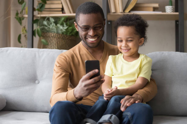 istock Smiling black father and son watch video on smartphone 1174255171