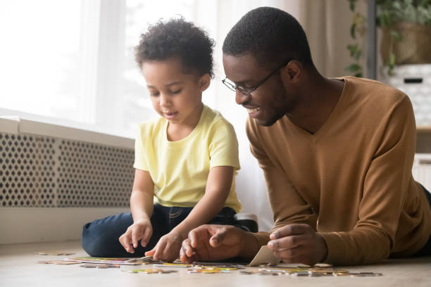 istock Black dad and little son assemble jigsaw puzzle together 1174255206