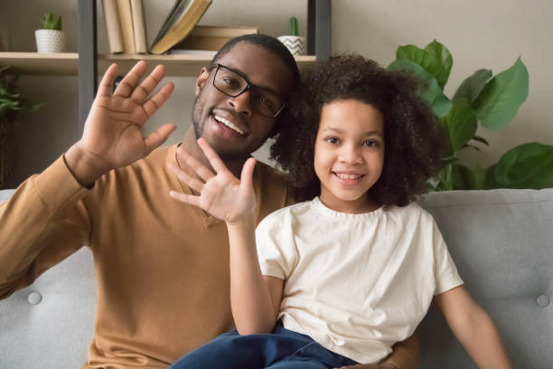smiling black dad and daughter wave talking on webcam - babies and children close up horizontal looking at camera imagens e fotografias de stock