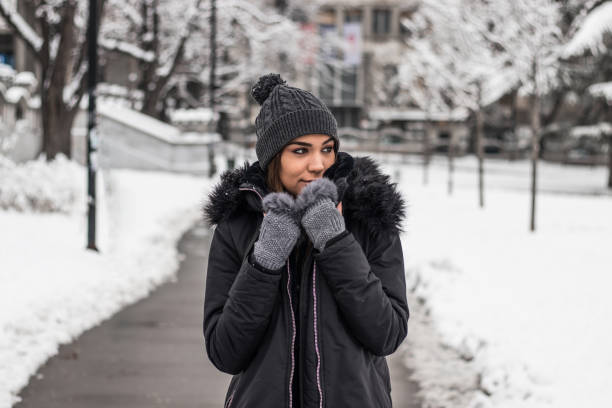 Beautiful young woman in warm clothing standing in park covered with snow.