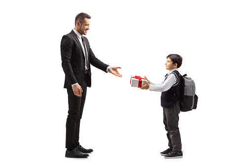 Full length profile shot of a schoolboy giving a present to a man in a suit isolated on white background