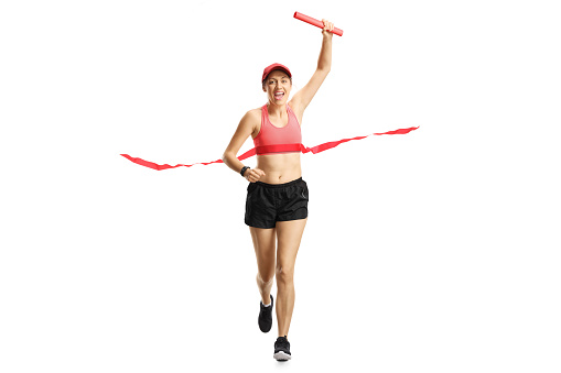 Full length portrait of a young woman carrying a red baton and finishing a relay race isolated on white background