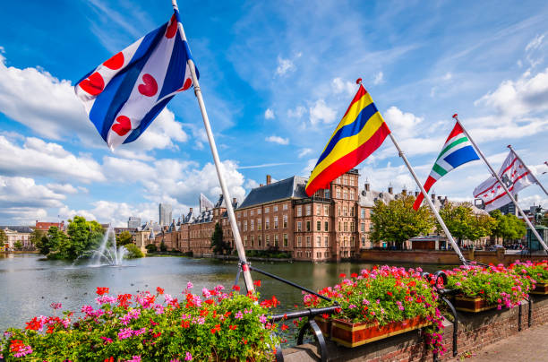 Flags of the Dutch provinces at the Hofvijver in The Hague, The Netherlands. Bright and colorful image with different flags of the Dutch provinces and flowering plants on the railing of the Court Pond (Hofvijver) at the parliament building on the Inner Court (Binnenhof). Blue sky with clouds background. Holiday and travel concept of the Hague, Netherlands. binnenhof photos stock pictures, royalty-free photos & images