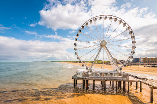 Bright and colorful image of Scheveningen beach with ferris wheel and pier at the coastline. North sea travel and tourism concept. A blue sky and white clouds on a summer day early in september.