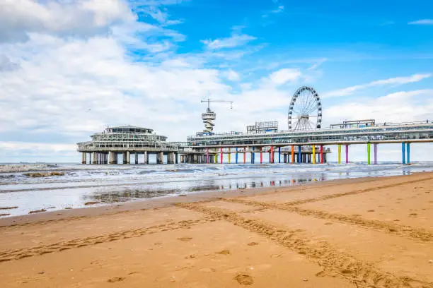Bright and colorful image of Scheveningen beach with ferris wheel and pier at the coastline. North sea travel and tourism concept. A blue sky and white clouds on a summer day early in september.