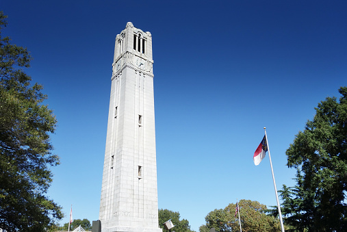 The belltower on the campus of NC State University in Raleigh North Carolina with the State flag