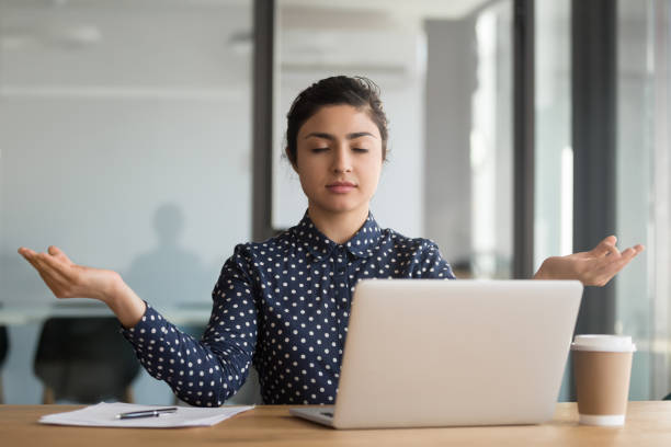 calm serene office worker indian woman resting meditating at workplace - yoga business women indoors imagens e fotografias de stock