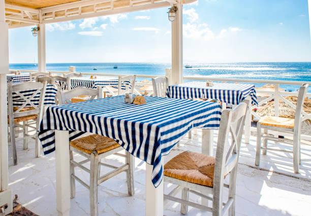 Beautiful view over traditional Greek tavern tables, blue sea and sky on the background. Food trip to Greece, Santorini concept. Beautiful view over traditional Greek tavern tables, blue sea and sky on the background. Food trip to Greece, Santorini concept. beach bar stock pictures, royalty-free photos & images