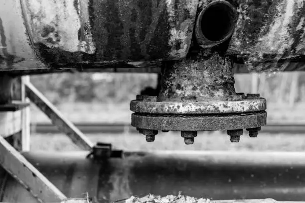 Old rustic metal pipe system with tightened flange outlet for drainage of oil or water, in closeup black and white industrial background concept