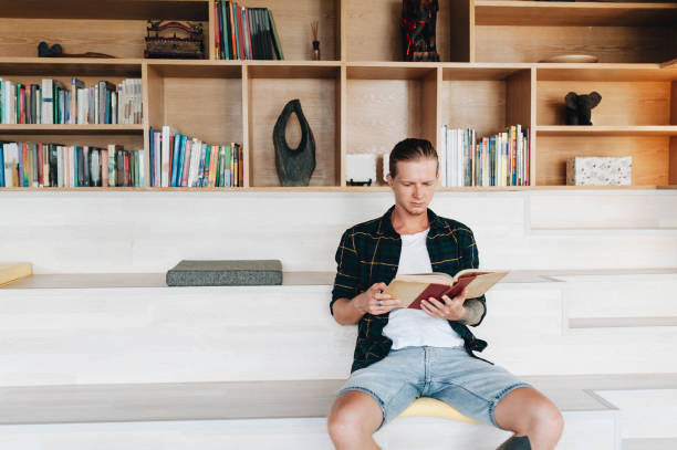 istock Serious male student reading a book in a library 1174265031