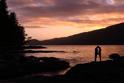 Silhouette romantic couple kissing on rock formation by sea. Full length of man and woman are enjoying sunset. They are spending leisure time together.