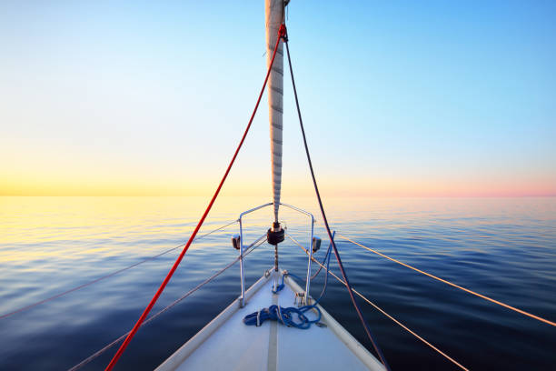 The calm water. White yacht sailing at sunset. A view from the deck to the bow, mast and the sails. Baltic Sea, Latvia The calm water. White yacht sailing at sunset. A view from the deck to the bow, mast and the sails. Baltic Sea, Latvia calm water photos stock pictures, royalty-free photos & images