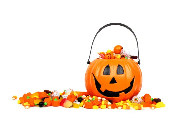 Halloween Jack o Lantern bucket overflowing with candy, side view isolated on a white background