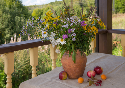Still life: Bouquet of wildflowers in clay vase and fruits